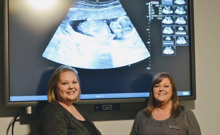 Toccoa Life ultrasound technician Kendra Scott (left) and Toccoa Life director Amanda Brothers stand in front of an ultrasound image.