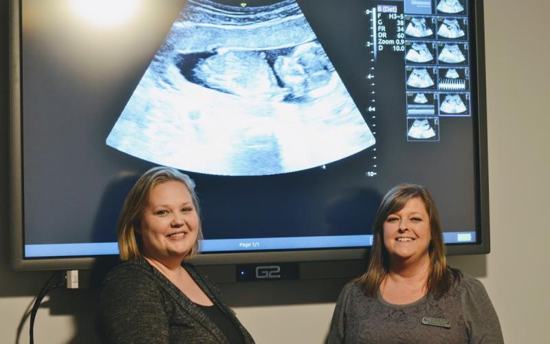 Toccoa Life ultrasound technician Kendra Scott (left) and Toccoa Life director Amanda Brothers stand in front of an ultrasound image.