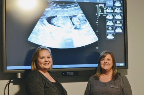 Toccoa Life ultrasound technician Kendra Scott (left) and Toccoa Life director Amanda Brothers stand in front of an ultrasound image.